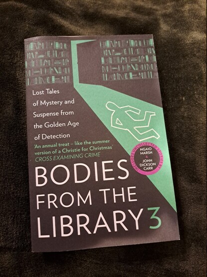 The book "Bodies from the Library 3" over a dark green blanket.