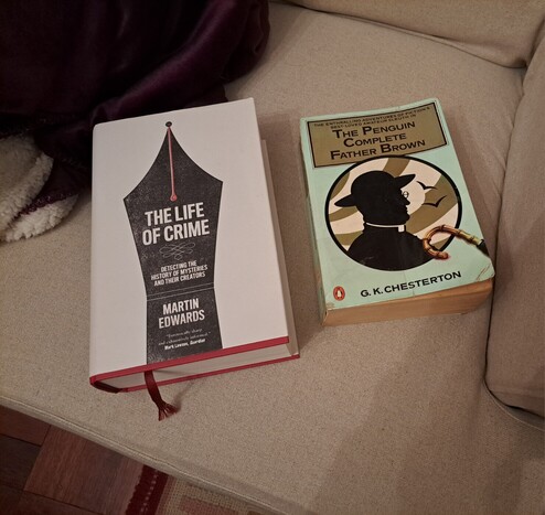 Two books: The Life of Crime and The Penguin Complete Father Brown in an armchair next to a blanket