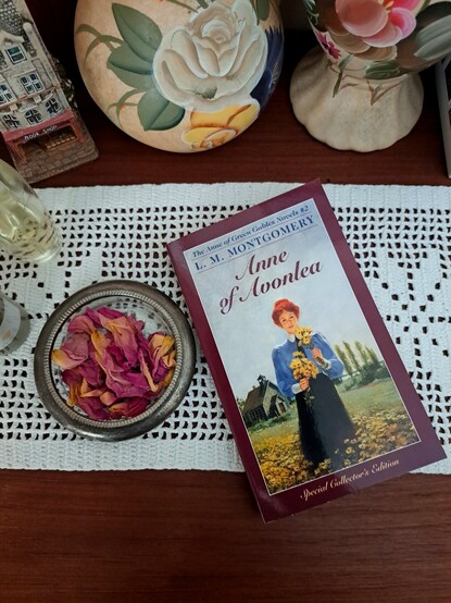 A book, some floral vases, a small plate with rose petals over a white crochet doily