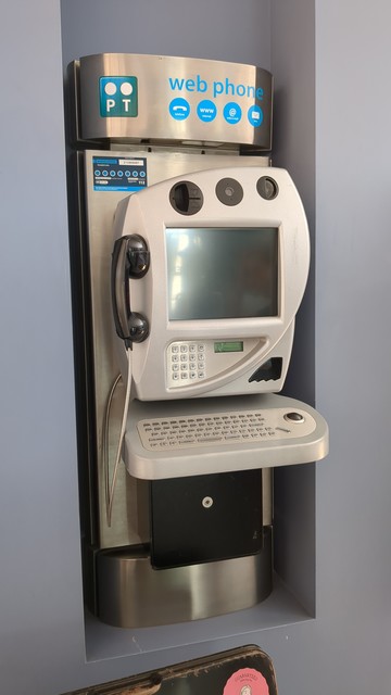 Um telefone público com um ecrã de cerca 14 polegadas, uma webcam, um teclado qwerty de tamanho real e uma trackball. 
Na parte superior encontra-se o logo da PT e o título "web phone" em letras azuis minúsculas.