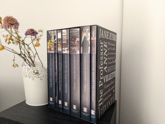A box of books by the Brontës next to a white vase with dried flowers