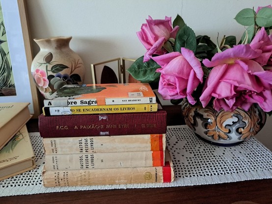 A book stack over a wood table with a vase with pink roses on the side