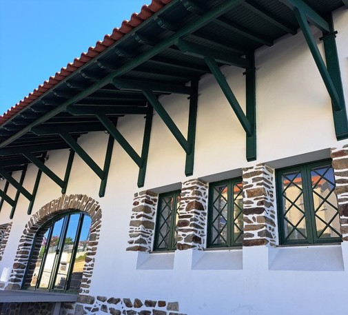 A white building with green windows decorated with stone and a wood green structure that supports the roof
