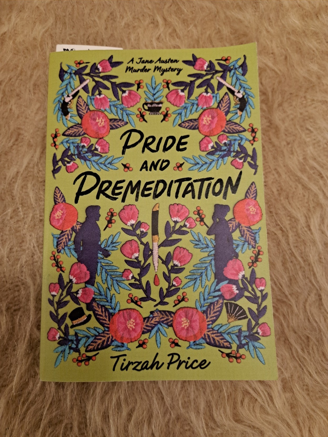 The cover of the paperback edition of &ldquo;Pride And Premeditation&rdquo;, which is &ldquo;A Jane Austen Murder Mystery&rdquo;, by Tirzah Price.  The cover is green, covered with flowers and the occasional hat, firearm, knife and teacup. There is also the silhouette of a man and a woman facing each other.