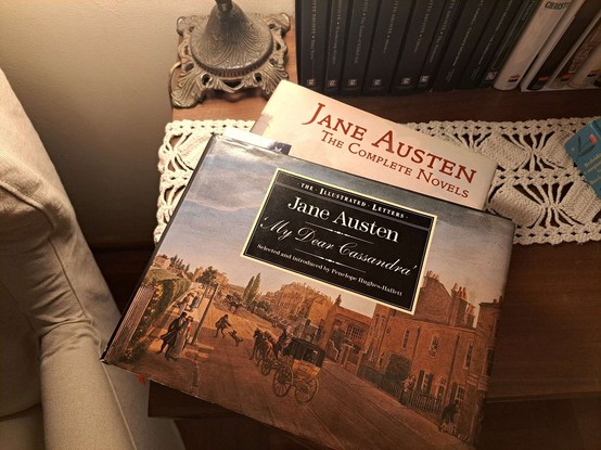 A book with the letters of Jane Austen, illustrated, over a book with the complete novels next to lamp turn on