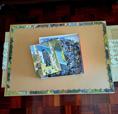A cardboard from a frame with a puzzle border completed and a box with puzzle pieces in the centre