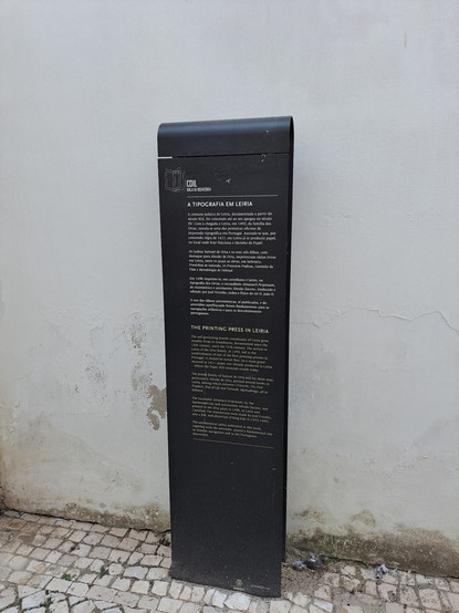 A black metal sign with some history about the place reading:
THE PRINTING PRESS IN LEIRIA
The self-governing Jewish community of Leiria grew steadily from its foundation, documented since the 13th century, until the 15th century. The arrival to Leiria of the Orta family, in 1492, led to the establishment of one of the first printing presses in Portugal. It should be noted that, by a royal grant received in 1411, paper was already produced in Leiria where the Paper Mill museum stands today. The Jewish family of Samuel A Orta and his three sons, particularly Abraão de Orta, printed several books in Leiria, among which Solomon's Proverbs, The First Prophets, Way of Life and Talmudic Methodology, all in Hebrew.
The incunable Almanach Perpetuum, by the
mathematician and astronomer Abraão Zacuto, was printed in the Orta press in 1496, in Latin and Castilian. The translations were made by José Vizinho also a Jew, and physician of king João 1 (1455-1495). The astronomical tables published in this book, together with the astrolabe, played a fundamental role in Atlantic navigation and in the Portuguese discoveries.