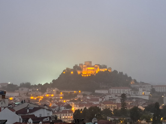 A view to a castle on a hill at a foggy night and the city lights at the bottom of the hill