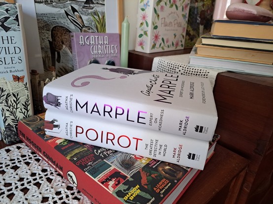 Two books, Marple and Poirot, Over another book surrounded by other books, a green candle.
