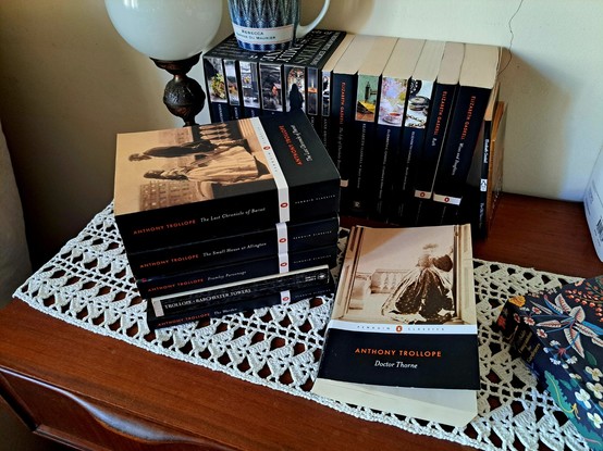 The six books of the Chronicles of Barsetshire over a wooden table next to other books and a lamp