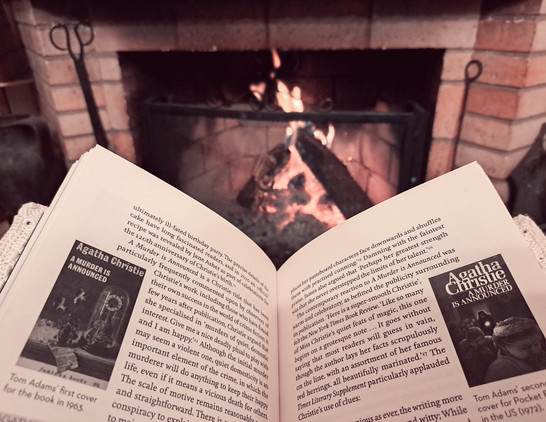 The book Marple Expert on Wickedness opened showing some text and covers of Miss Marple books in front of an open fire