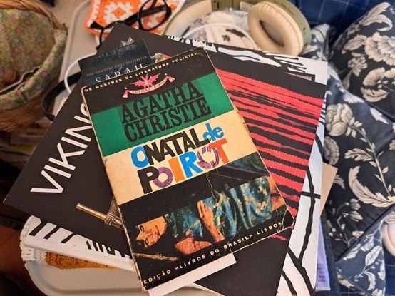 A book on top of other books next to reading glasses, headphones, a basket with nuts and pillows