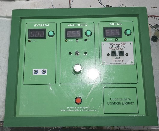 Painel de seleção de fontes para maquete de ferromodelismo, projetado e construído por Ernesto S. Jr. O painel tem 4 áreas principais. As 3 de cima são identificadas como Externa, Analógico e Digital. Cada uma delas tem um botão verde com um led embutido, e um voltímetro. Elas também têm outros controles. A área inferior tem apenas um botão vermelho com led, para ligar ou desligar a alimentação da linha.