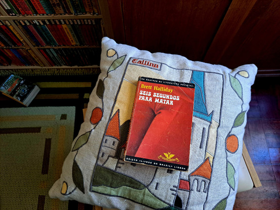A book with a red cover over a pillow with more books in a shelf
