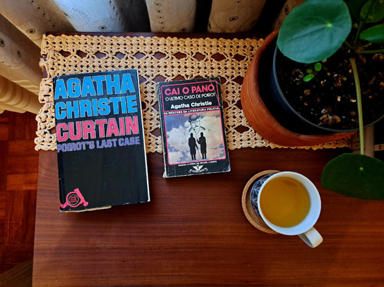 An English and Portuguese edition of Curtain over a wooden table with a cup of tea and a plant vase