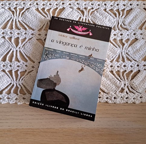A book cover in blue tones with a bridge and two figures, one taking to the river where there's some boats. Three book is vengeance is mine by Mickey Spillane