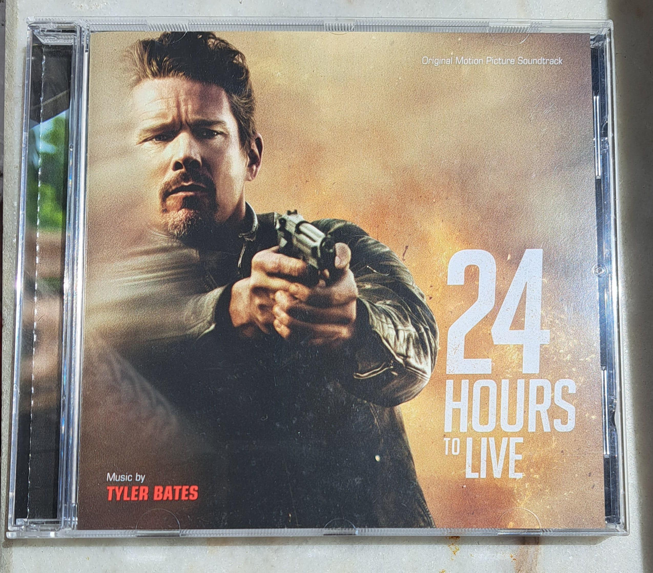 Foto do CD da banda sonora do filme "24 Hours to Live", que diz "Music by Tyler Bates". A capa mostra um senhor a apontar uma arma de fogo.