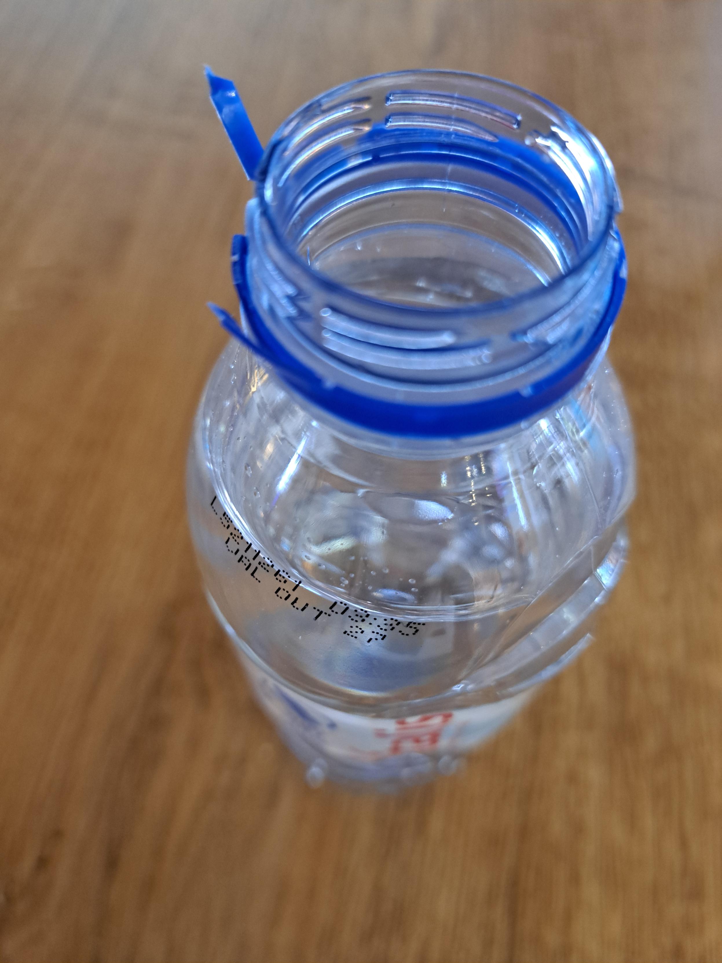 A plastic bottle of water, open and lidless, the plastic lid having been ripped off A plastic bottle of water, open and lidless, the plastic lid having been ripped off