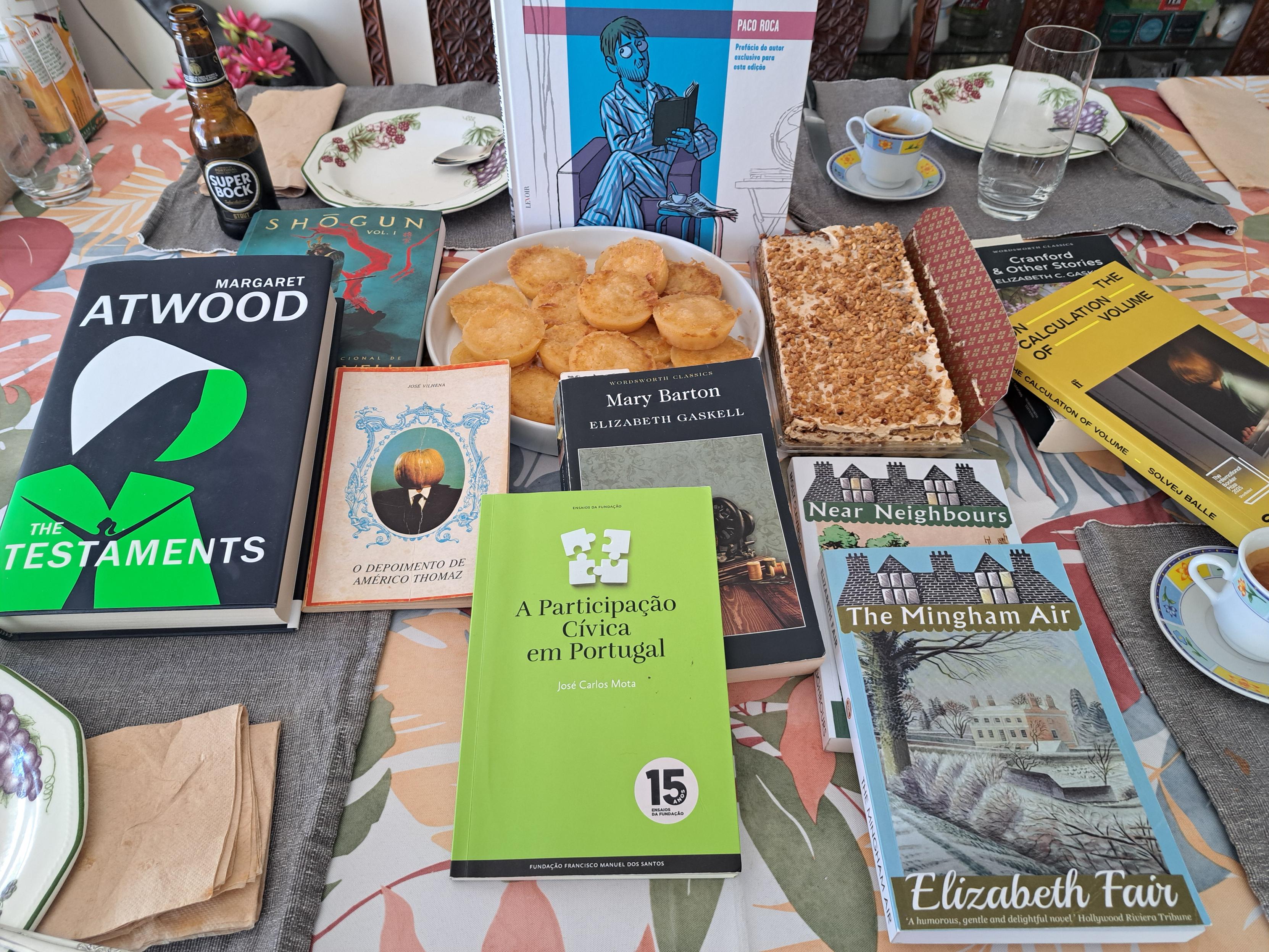 Books, Beers (só uma) e bolos (e cafés). 10 livros à mostra: * Memórias de um homem em pijama (Paco Roca) * Shogun Vol. 1 * The Testaments (Margaret Atwood) * O Depoimemto de Américo Thomaz (José Vilhena) * Mary Barton (Elizabeth Gaskell) * A Participação Cívica em Portugal (José Carlos Mota) * Near Neighbours (Molly Clavering) * The Mingham Air (Elizabeth Fair) * Cranford & Other Stories (Elizabeth Gaskell) * On The Calculation Of Volume I - Silvej Balle Uma Super Bock mini preta, três pratos de sobremesa com motivos de fruta, dois cafés em chávenas floridas. A toalha é em com folhas Outonais. Os bolos são de dois tipos: um prato com delícias sem lactose, e um bolo de bolacha.